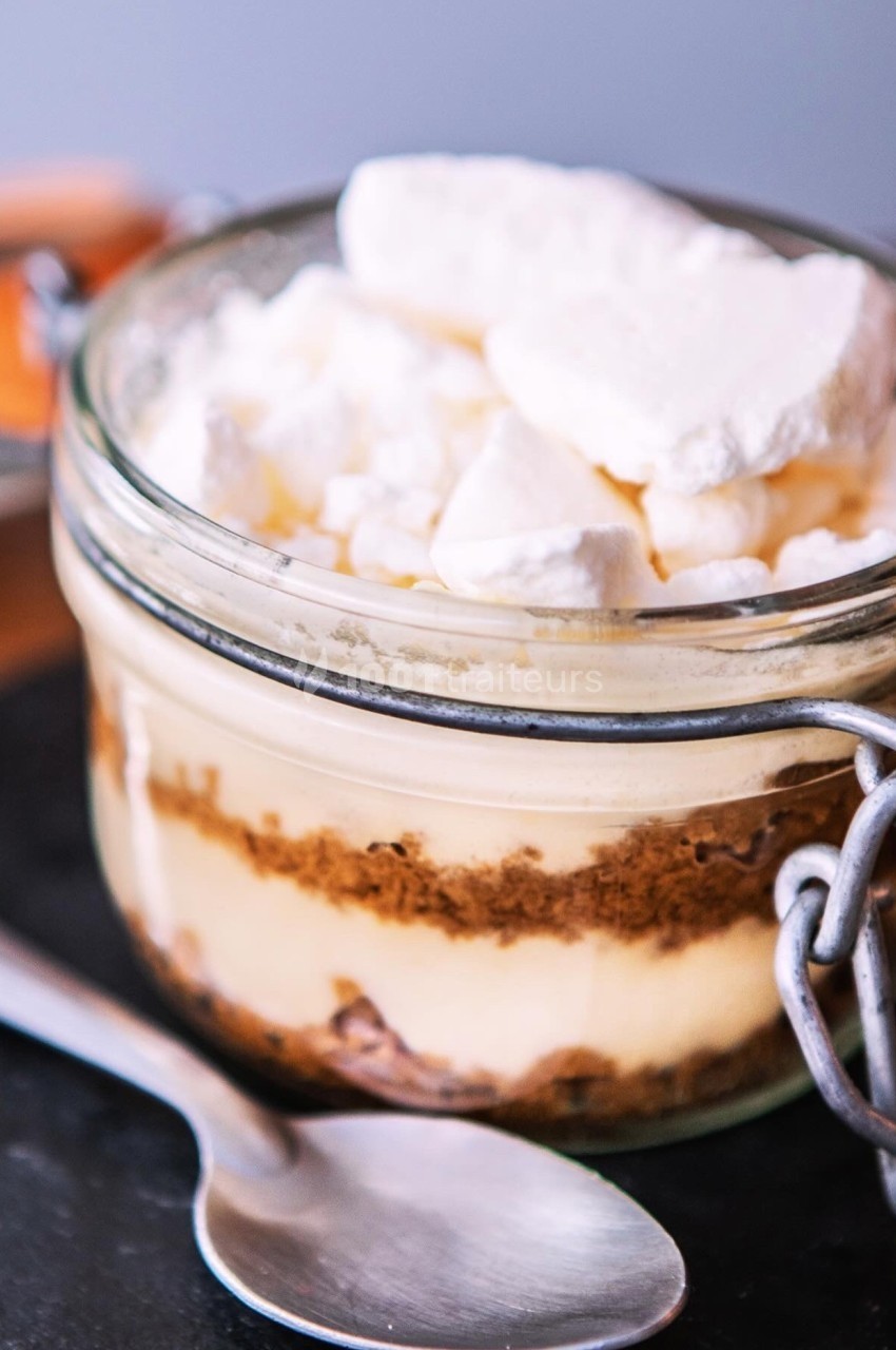 Dessert en verrine avec couches de crème, biscuit émietté et morceaux de meringue, présenté sur une ardoise.