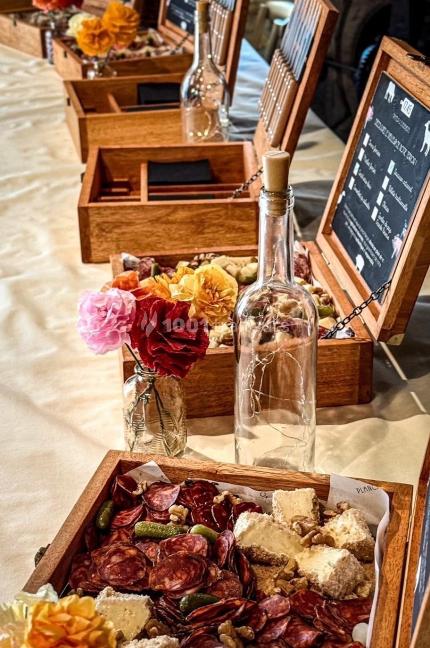 Plateaux en bois garnis de charcuterie, fromages et condiments, disposés sur une table avec des fleurs et une bouteille en…