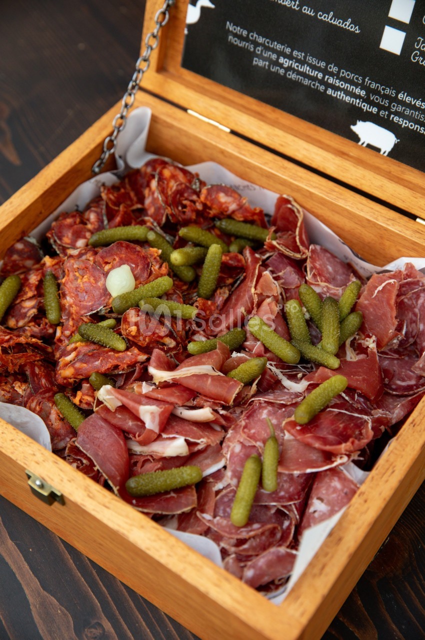 Plateau en bois contenant un assortiment de charcuteries et de cornichons, présenté sur du papier blanc.