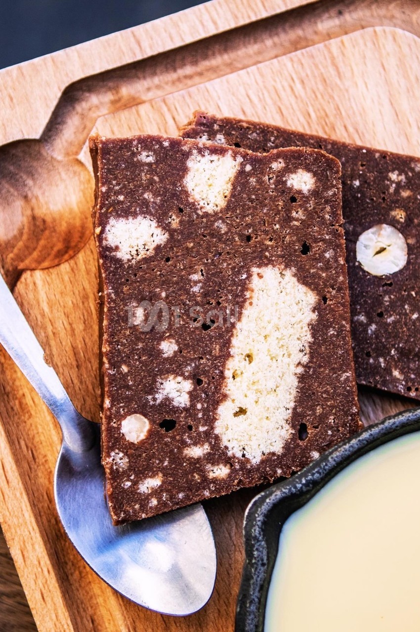 Tranches de gâteau marbré au chocolat et à la vanille sur une planche en bois, avec une cuillère et un bol de sauce.