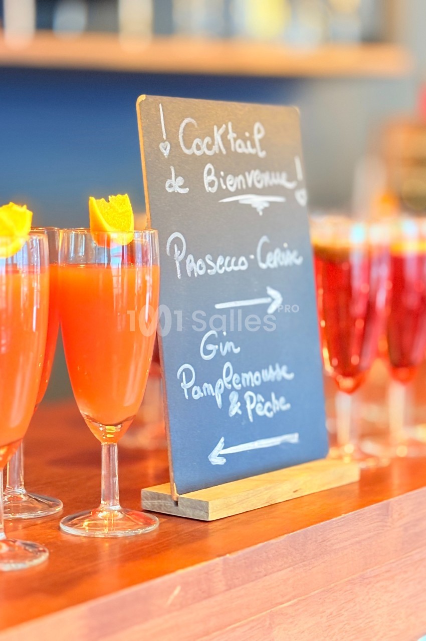 Ardoise indiquant deux choix de cocktails, avec des verres remplis de boissons colorées garnies d'écorces d'orange.