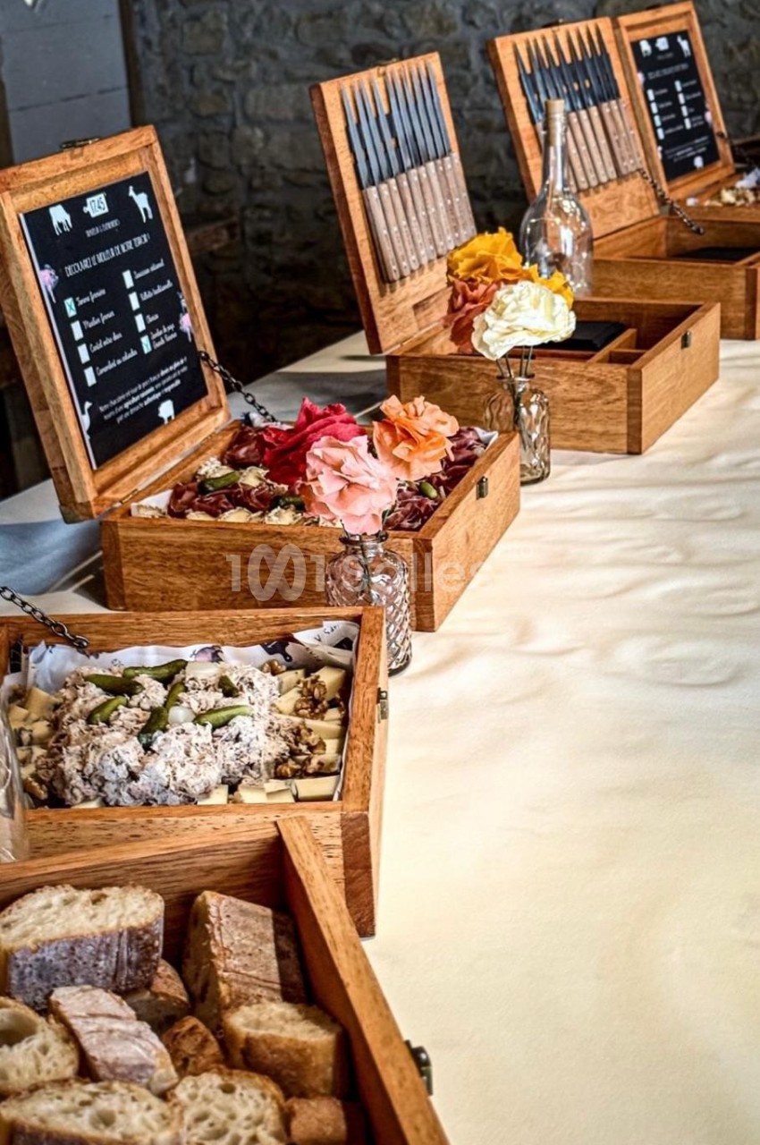 Plateau de dégustation avec pains, fromages, charcuteries et couteaux disposés dans des boîtes en bois sur une table.