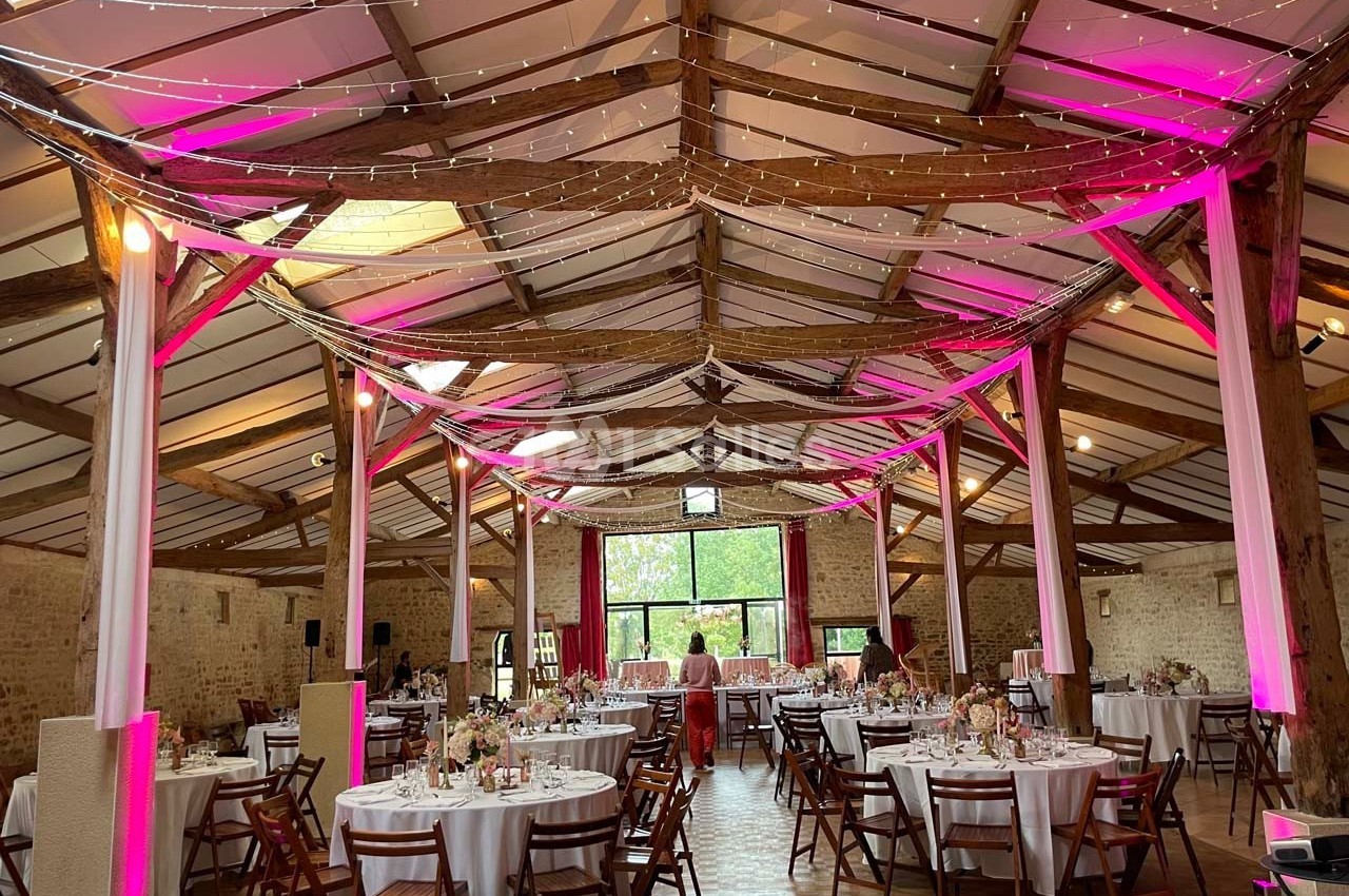 Salle de réception décorée avec des guirlandes lumineuses et des tables rondes dressées pour un événement festif.