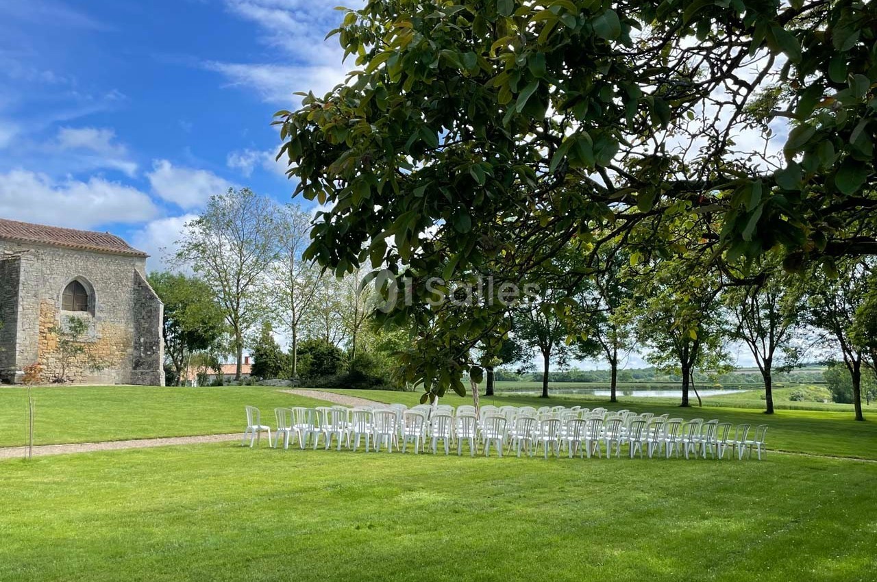 Chaises blanches alignées sur une pelouse verte près d'une église en pierre, entourées d'arbres sous un ciel partiellement…