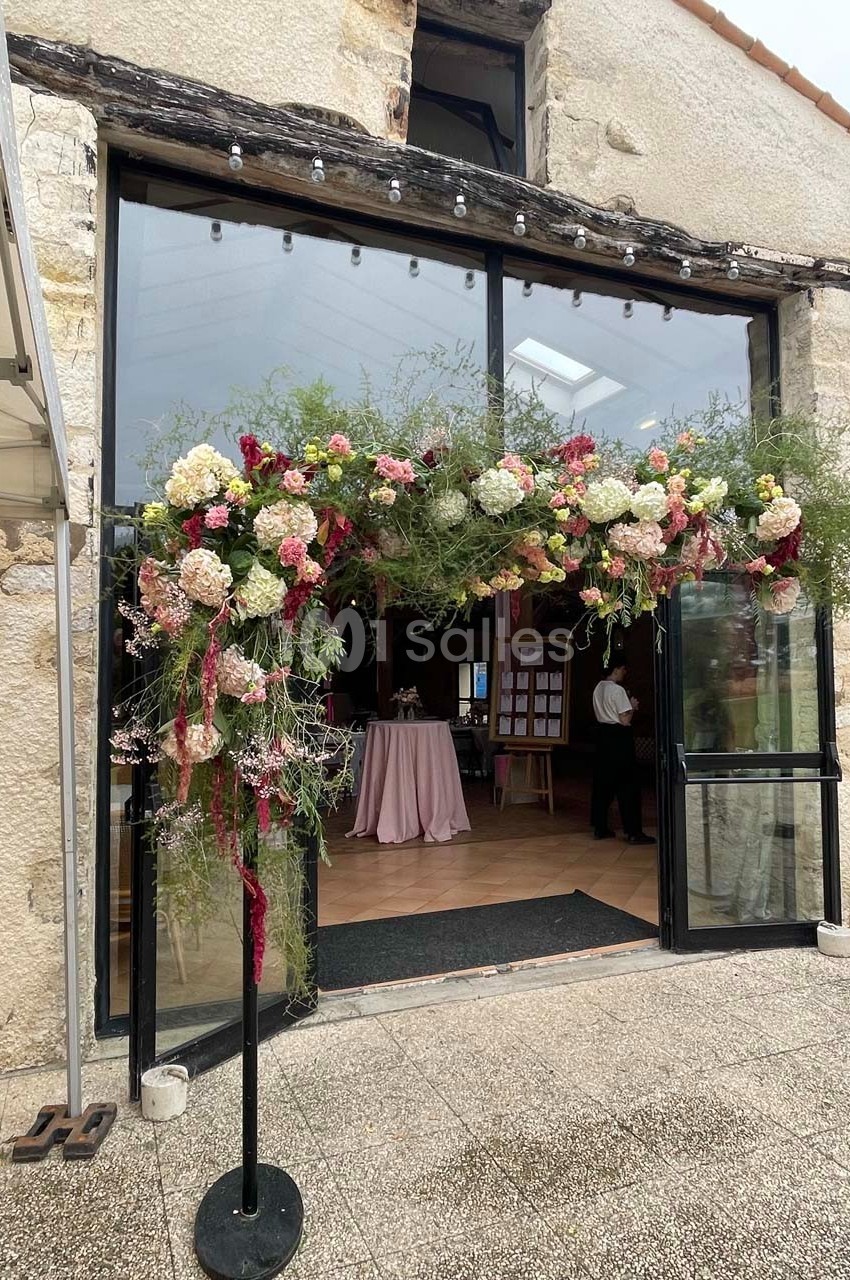 Entrée d'un bâtiment en pierre décorée d'une arche florale avec des fleurs colorées et feuillages.