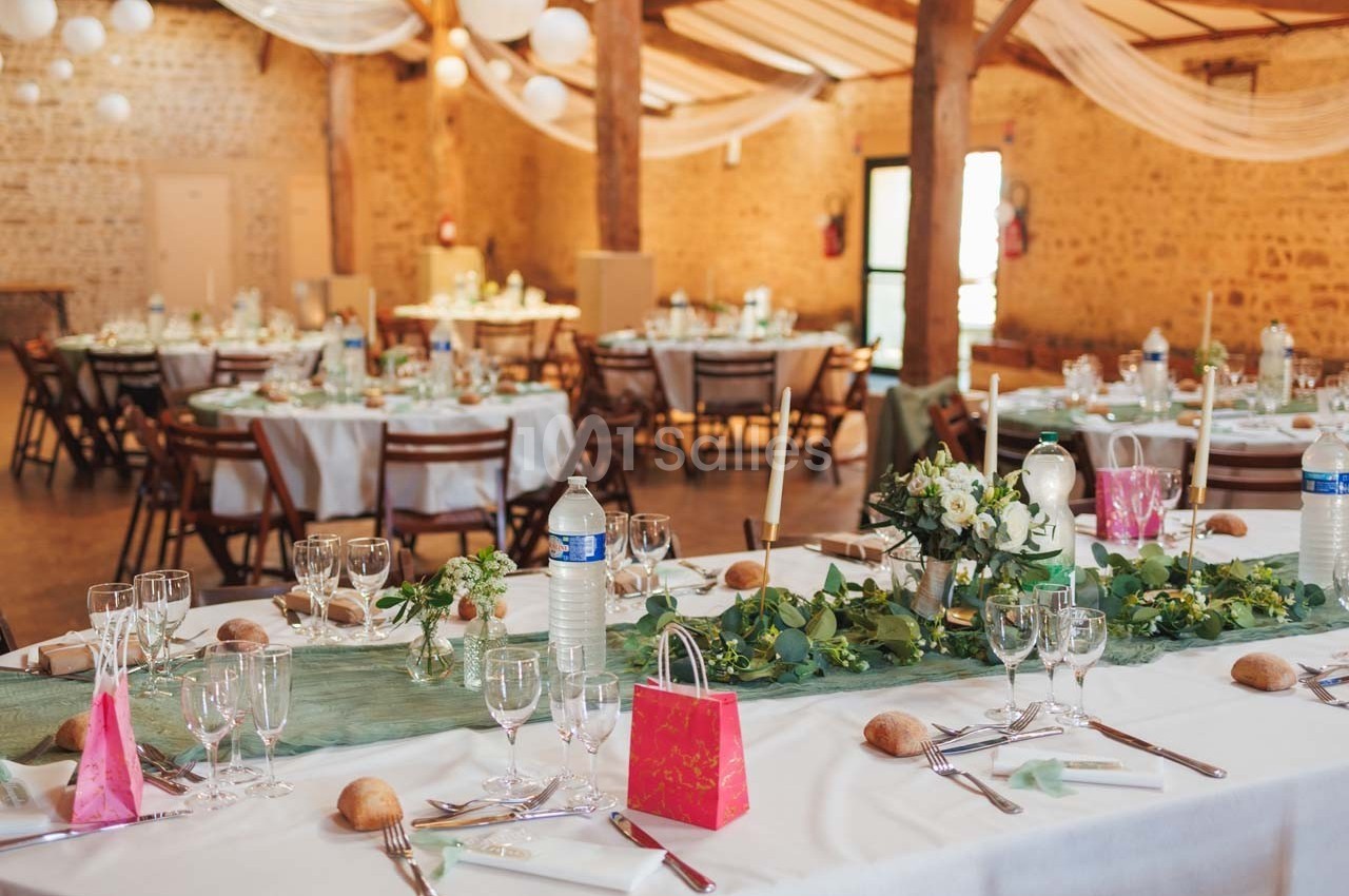 Salle de réception décorée pour un mariage avec tables dressées, nappes blanches, bouquets et éléments de décoration verts.
