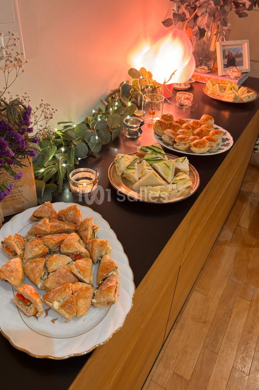 Assortiment de plats salés disposés sur un buffet en bois, décoré de guirlandes lumineuses et de fleurs.