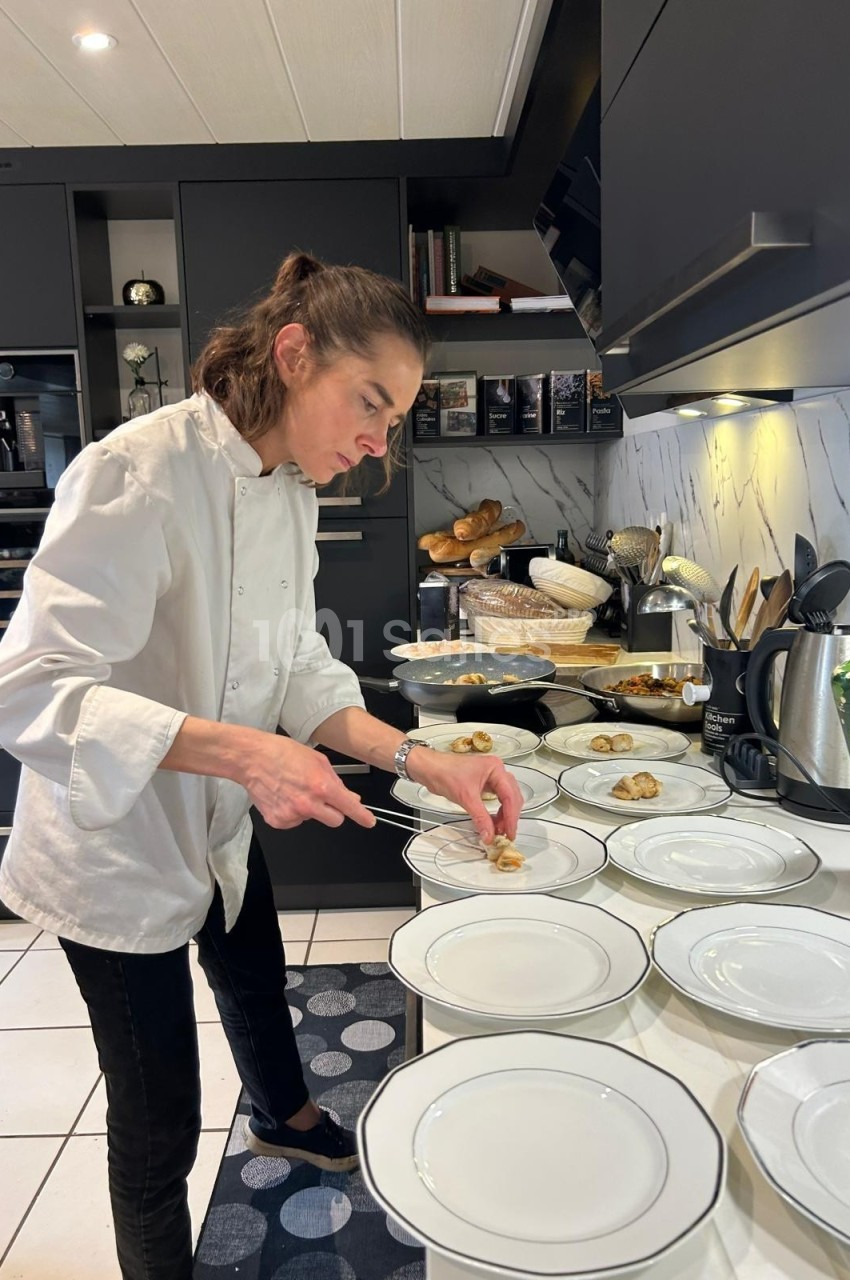 Une chef prépare des assiettes dans une cuisine moderne avec des plats et ustensiles disposés autour.