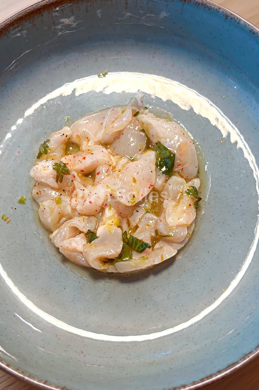 Assiette contenant un tartare de poisson cru assaisonné, servi dans un bol bleu sur une table en bois.