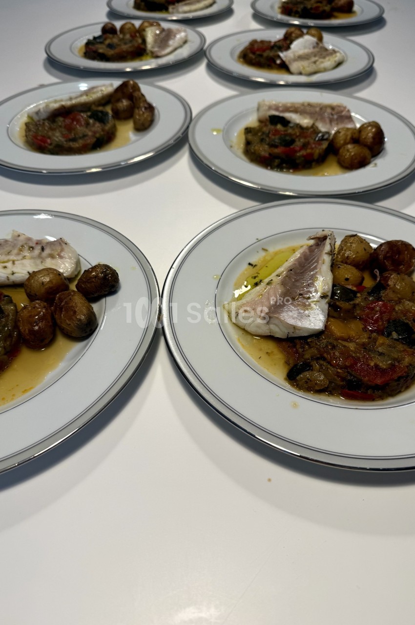 Assiettes garnies de poisson, légumes grillés et pommes de terre rôties, disposées sur une table blanche.