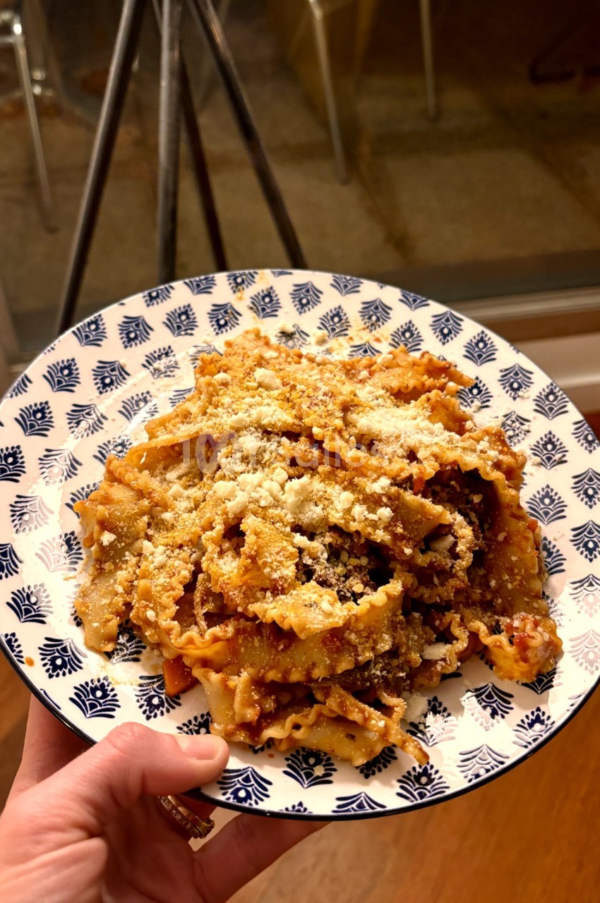 Assiette de pâtes à la sauce tomate garnies de fromage râpé, tenue à la main dans un intérieur éclairé.