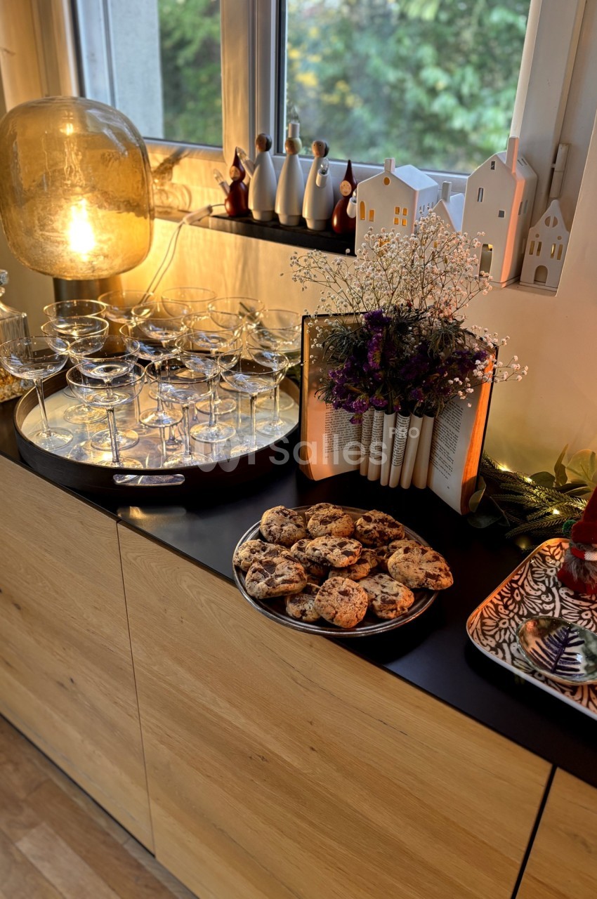 Buffet décoré avec des coupes en verre, des biscuits, des fleurs séchées et des figurines devant une fenêtre.