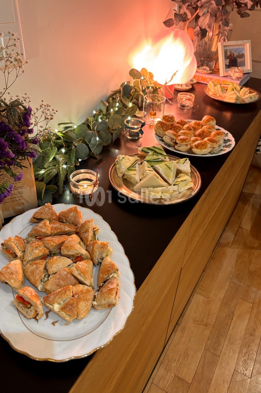 Plats variés de sandwichs et amuse-bouches disposés sur un buffet décoré de guirlandes lumineuses et de fleurs.