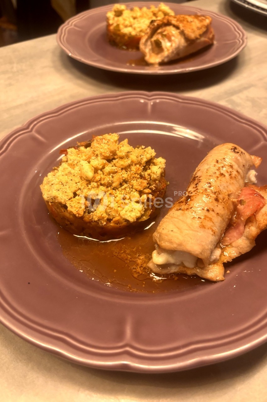 Assiette contenant un roulé de viande farci et une tomate garnie de crumble salé, servie sur une assiette violette.