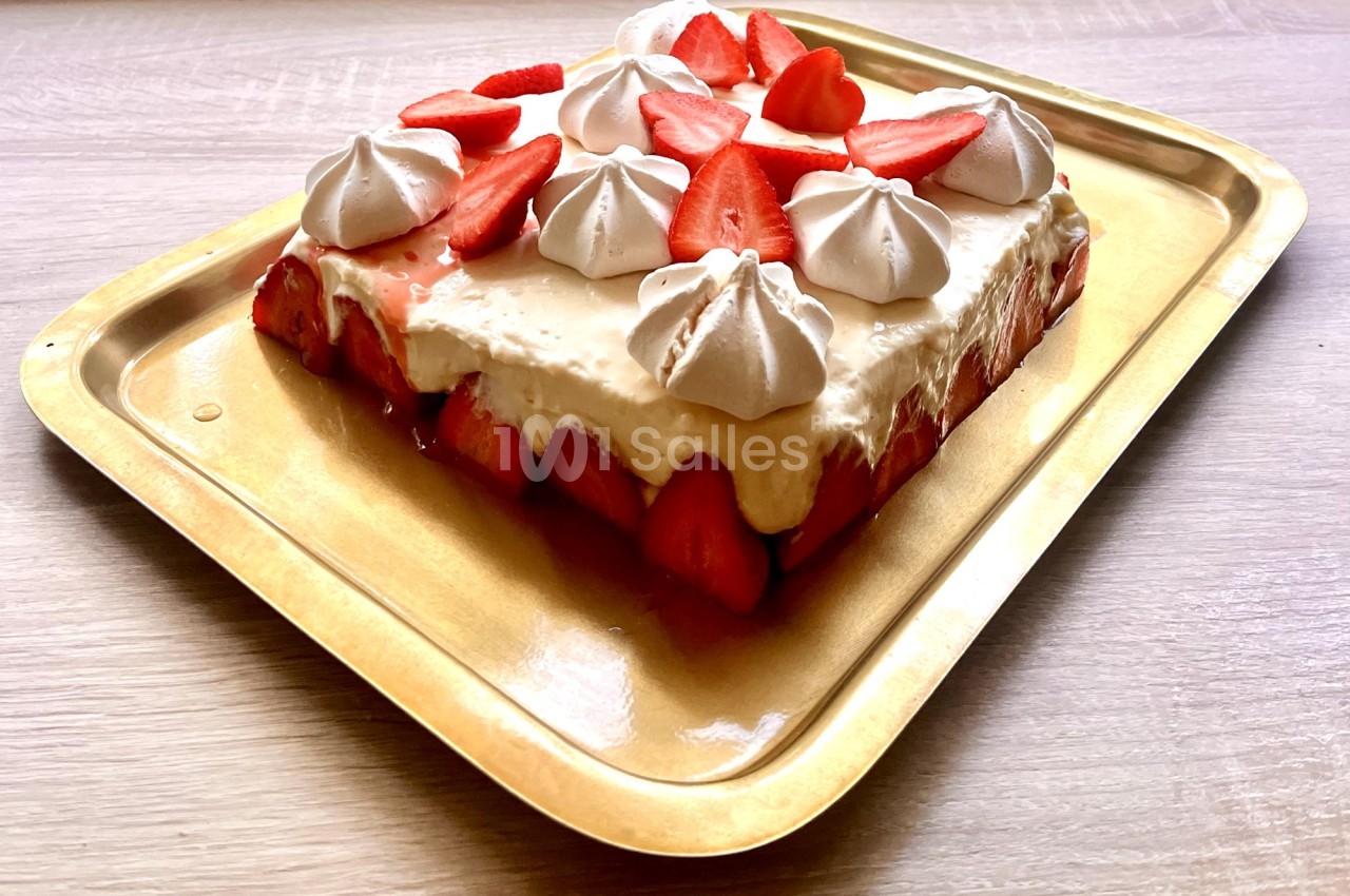 Gâteau décoré de fraises fraîches et de meringues blanches, présenté sur un plateau doré.