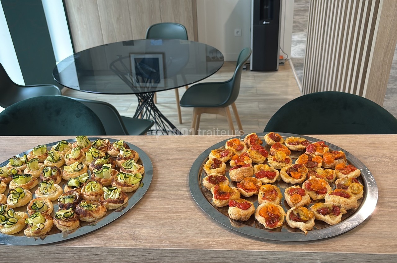 Plateaux de bouchées apéritives variées disposés sur un comptoir en bois dans une salle moderne avec table et chaises.