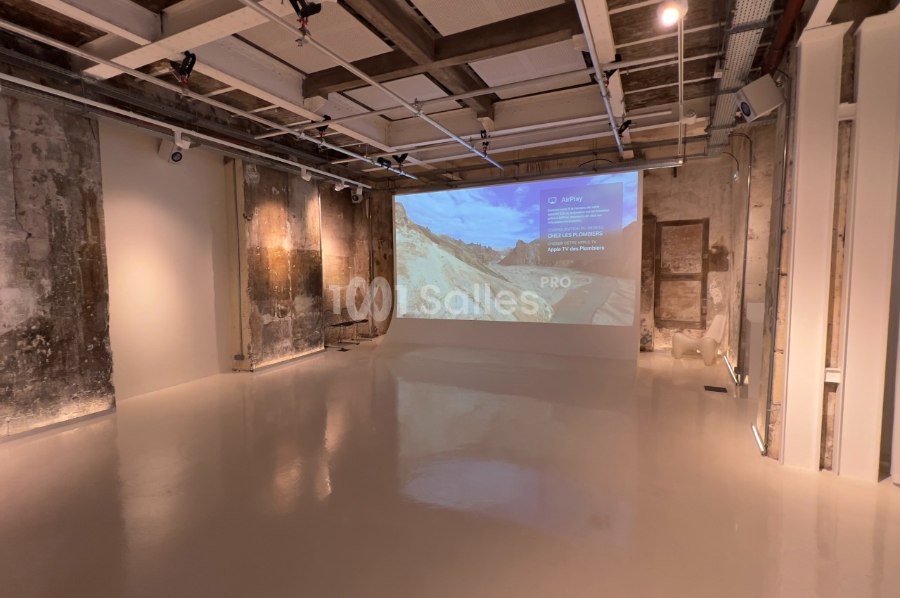 Salle minimaliste avec murs en béton brut, sol clair et projection d'une image sur un mur.