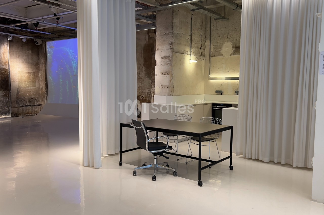 Espace intérieur moderne avec murs bruts, sol brillant, rideaux blancs et mobilier minimaliste.