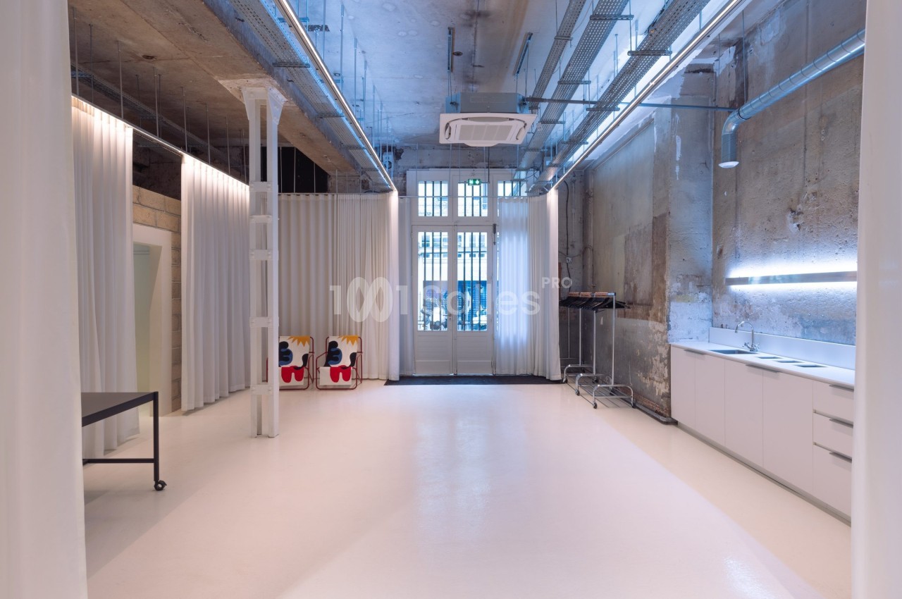 Intérieur d'un espace moderne avec murs bruts, sol clair, mobilier minimaliste et grandes fenêtres vitrées.