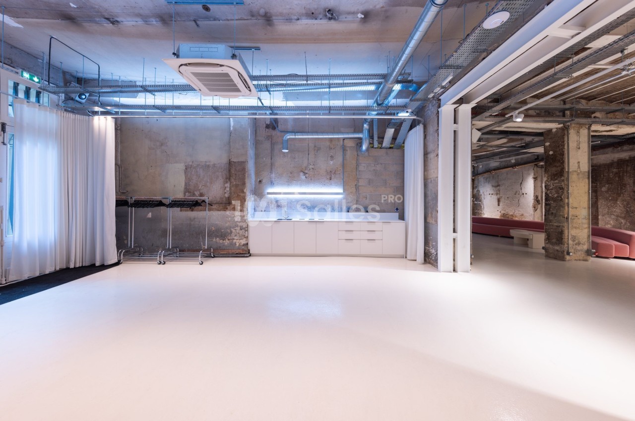 Espace intérieur industriel avec murs bruts, sol clair, éclairage moderne et mobilier minimaliste.