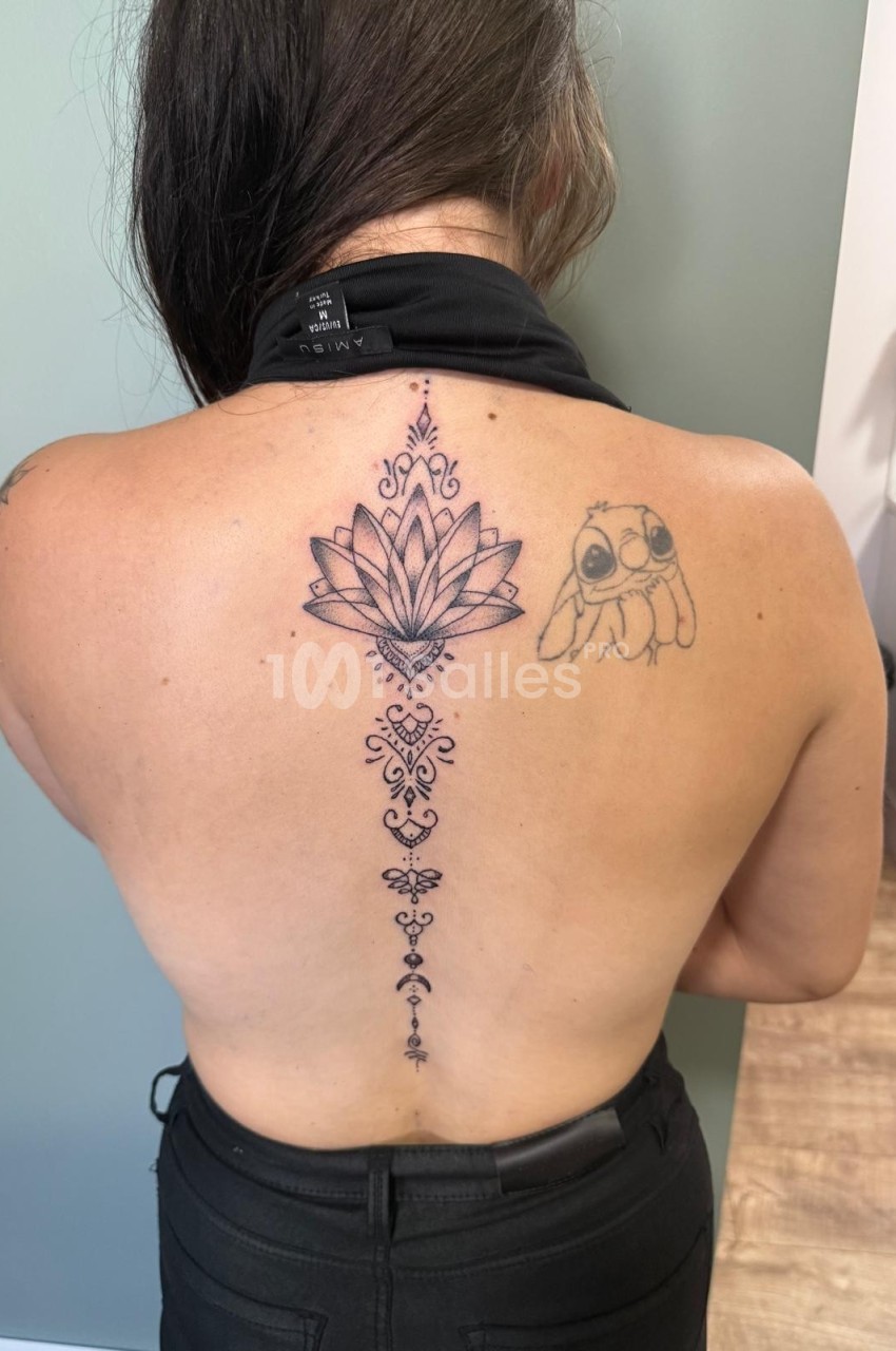 Femme de dos montrant un tatouage central de fleur de lotus et motifs ornementaux, avec un dessin d'animal à droite.