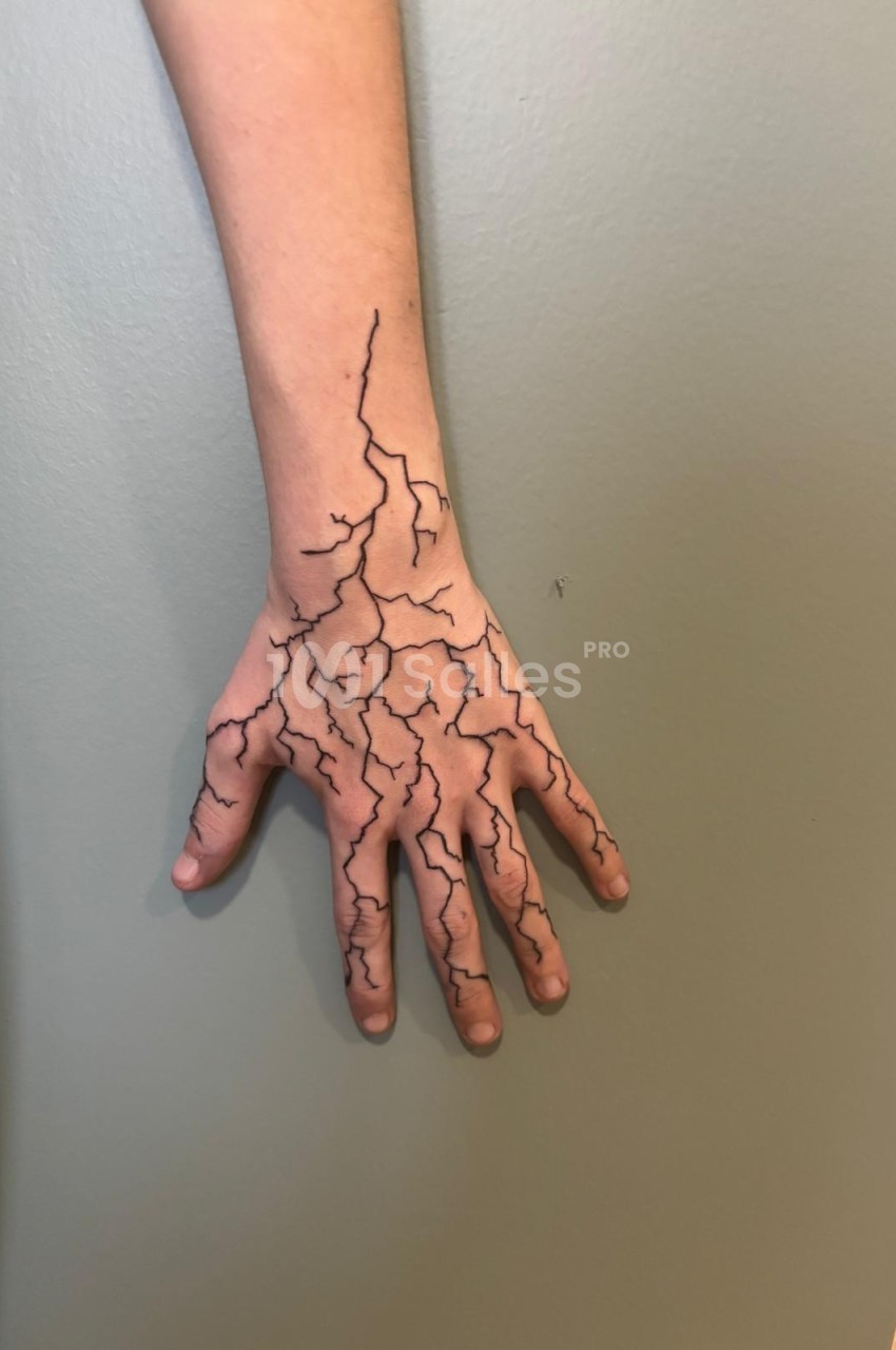 Bras et main avec un motif de fissures noires dessinées sur la peau, posé contre un mur beige.
