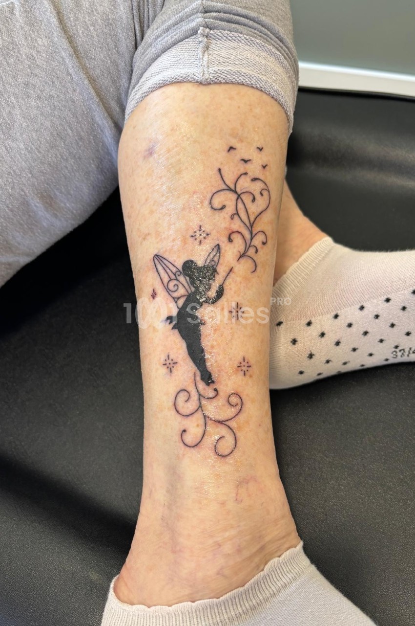 Tatouage sur une jambe représentant une fée noire entourée de motifs floraux et d'étoiles.