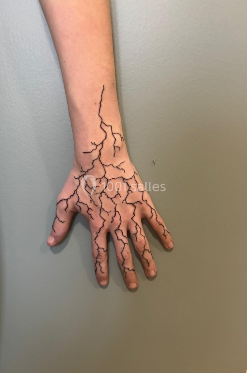 Bras et main avec un motif de fissures noires dessinées sur la peau, posé contre un mur gris.