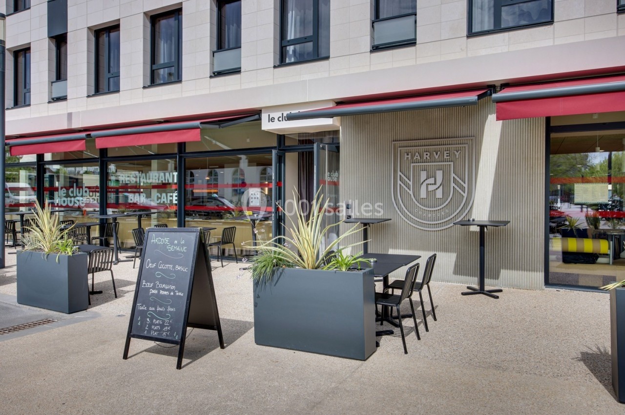 Façade d'un restaurant avec terrasse aménagée, tables, chaises, plantes en pot et ardoise affichant le menu.