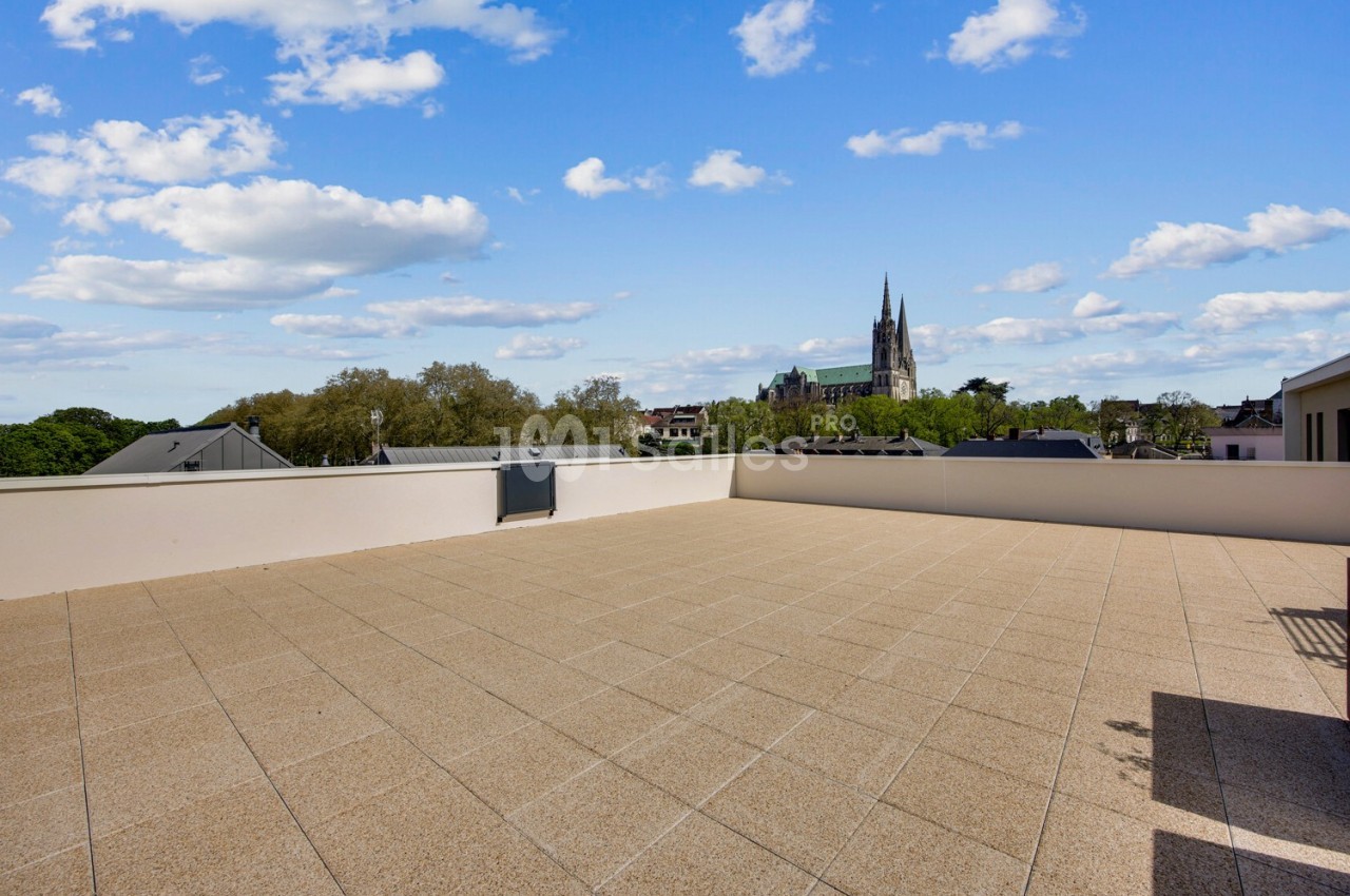 Terrasse spacieuse avec vue dégagée sur des toits, des arbres et une église au loin sous un ciel partiellement nuageux.