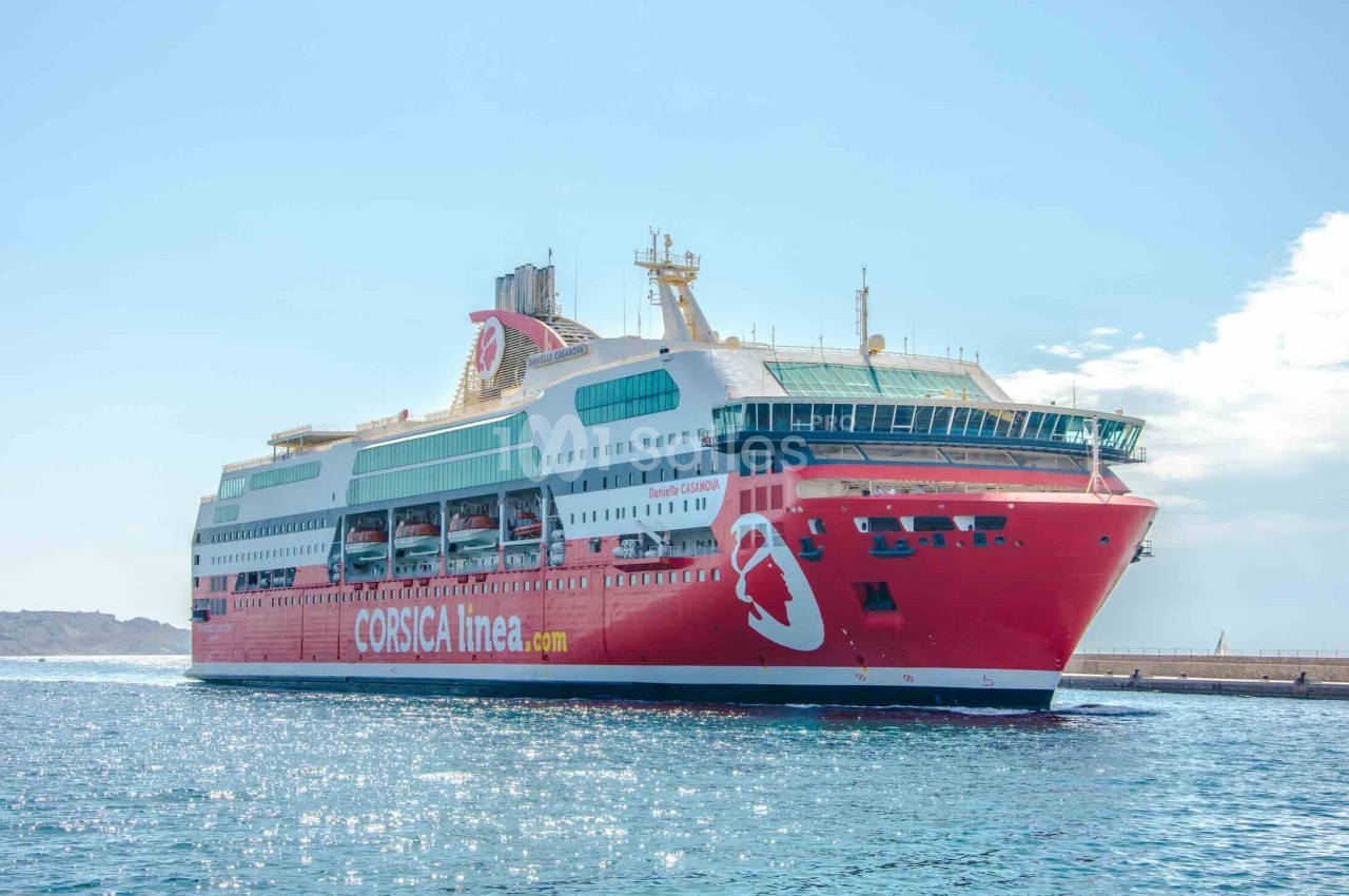 Ferry rouge de Corsica Linea naviguant sur une mer calme, avec un ciel dégagé en arrière-plan.