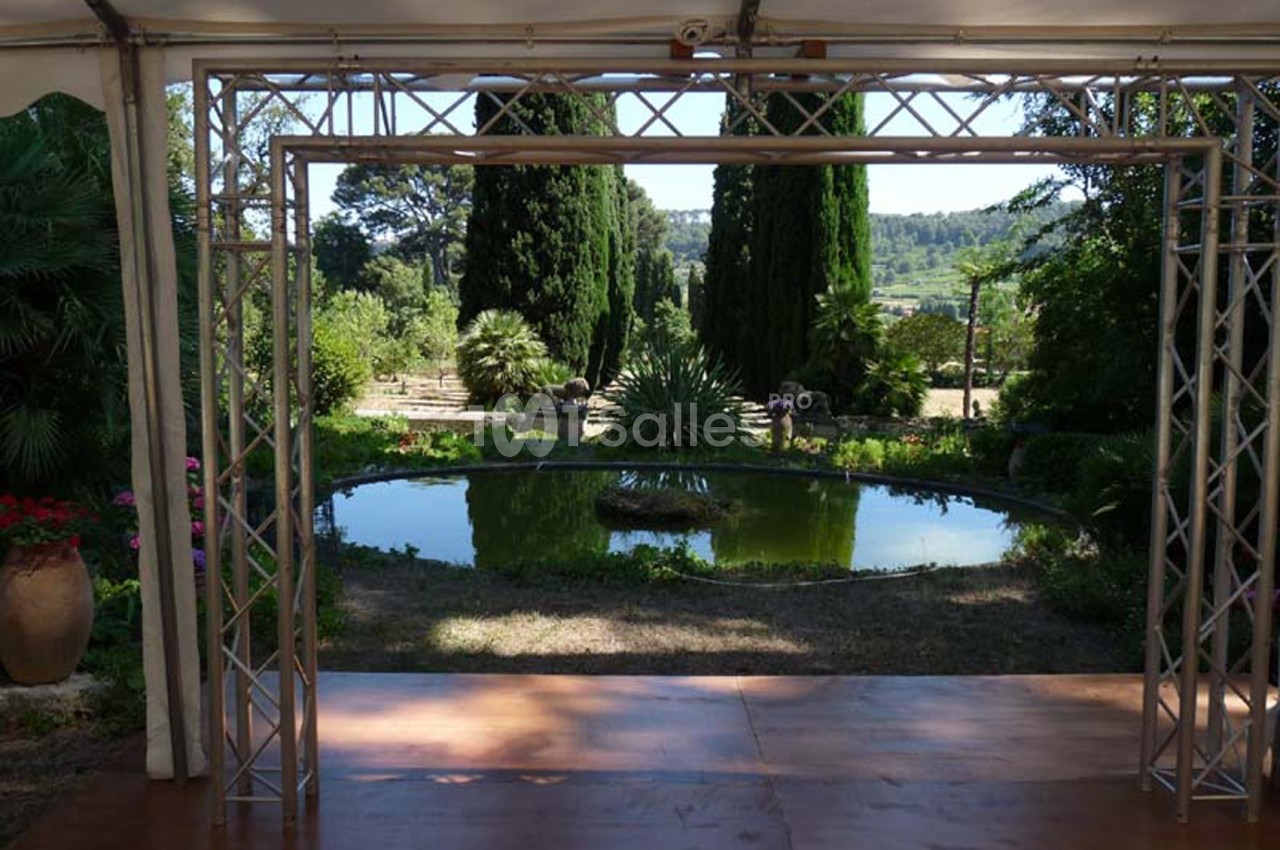 Vue d'un jardin avec un petit bassin rond entouré de végétation, encadré par une structure métallique.