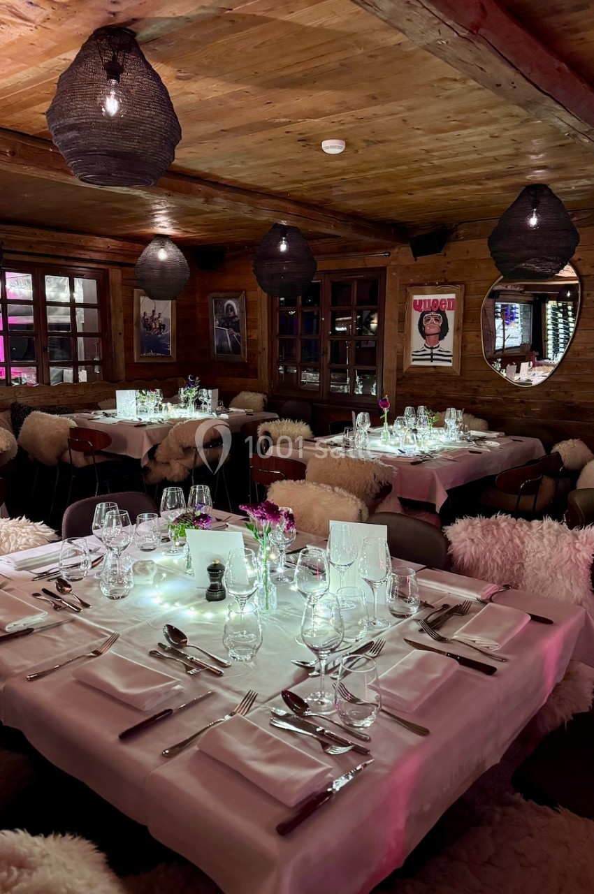Salle de restaurant chaleureuse avec tables dressées, nappes blanches, chaises couvertes de fourrure et éclairage tamisé.