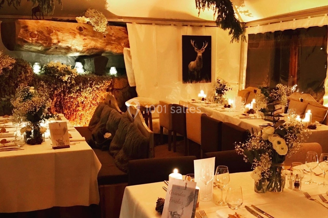 Salle de restaurant chaleureuse avec tables dressées, bougies allumées et décoration naturelle en bois et fleurs.