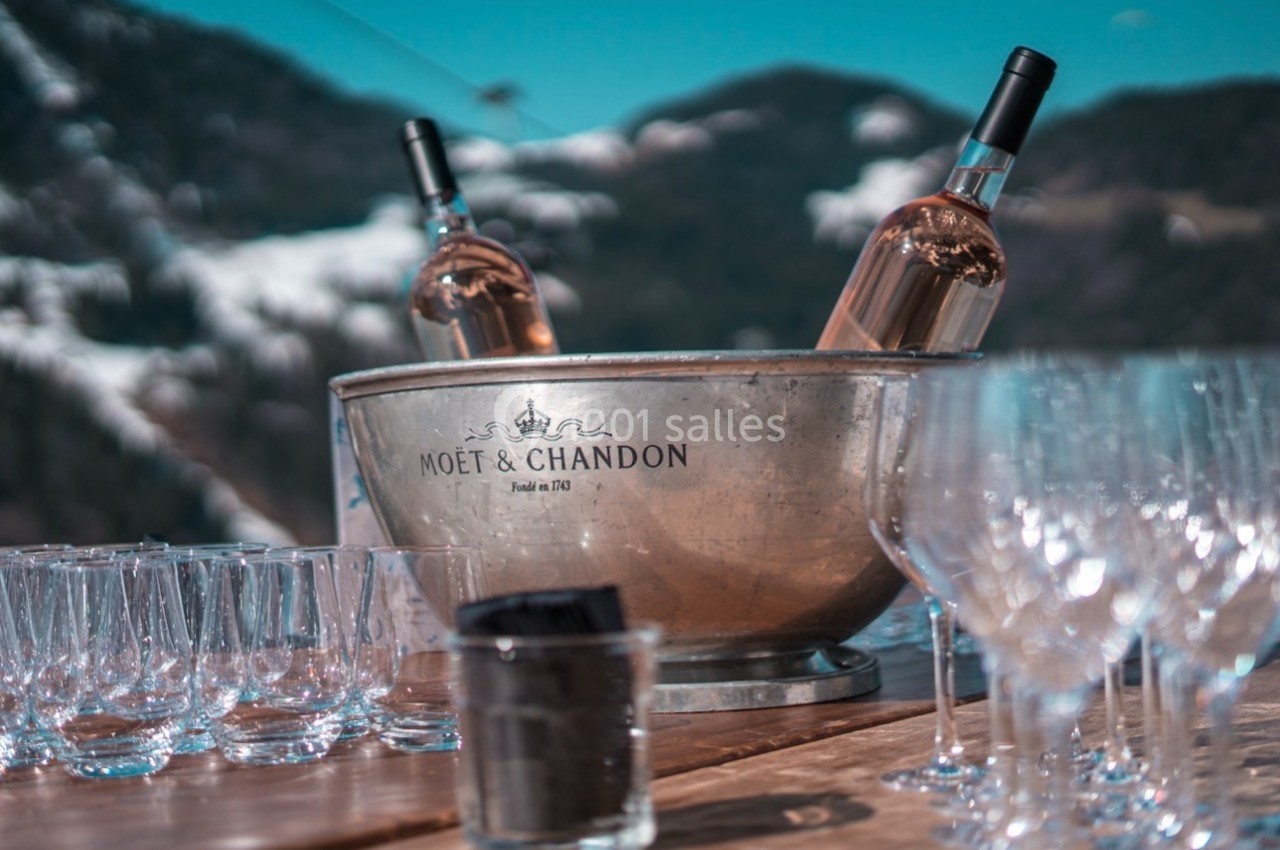 Seau à champagne Moët & Chandon avec deux bouteilles, entouré de verres sur une table en extérieur, vue sur montagnes…