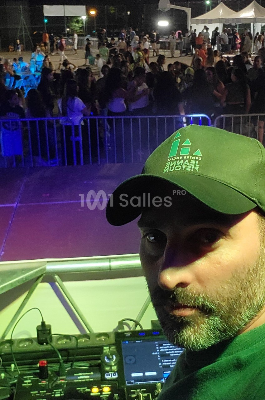Un DJ mixe sur une scène en plein air, face à une foule rassemblée pour un événement nocturne.