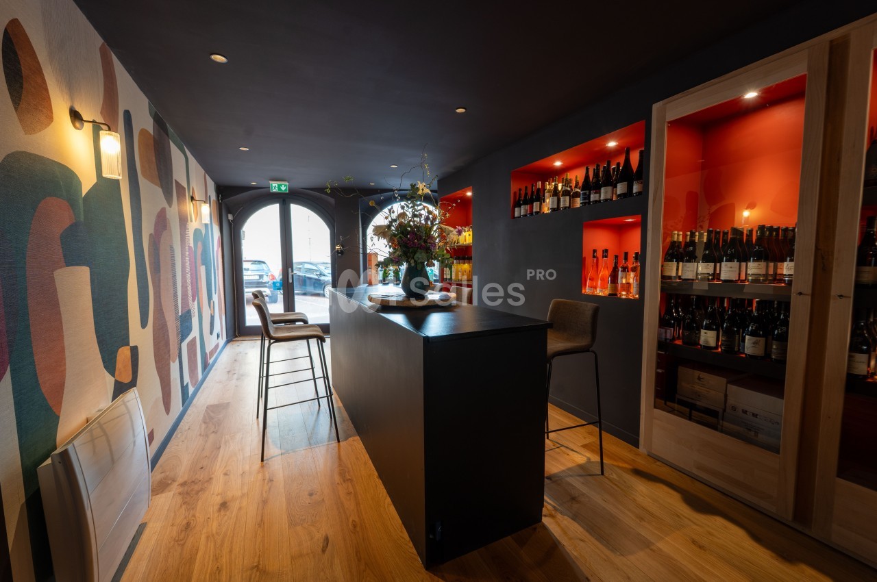 Intérieur d'un bar à vin moderne avec un comptoir central, étagères de bouteilles et décoration murale colorée.