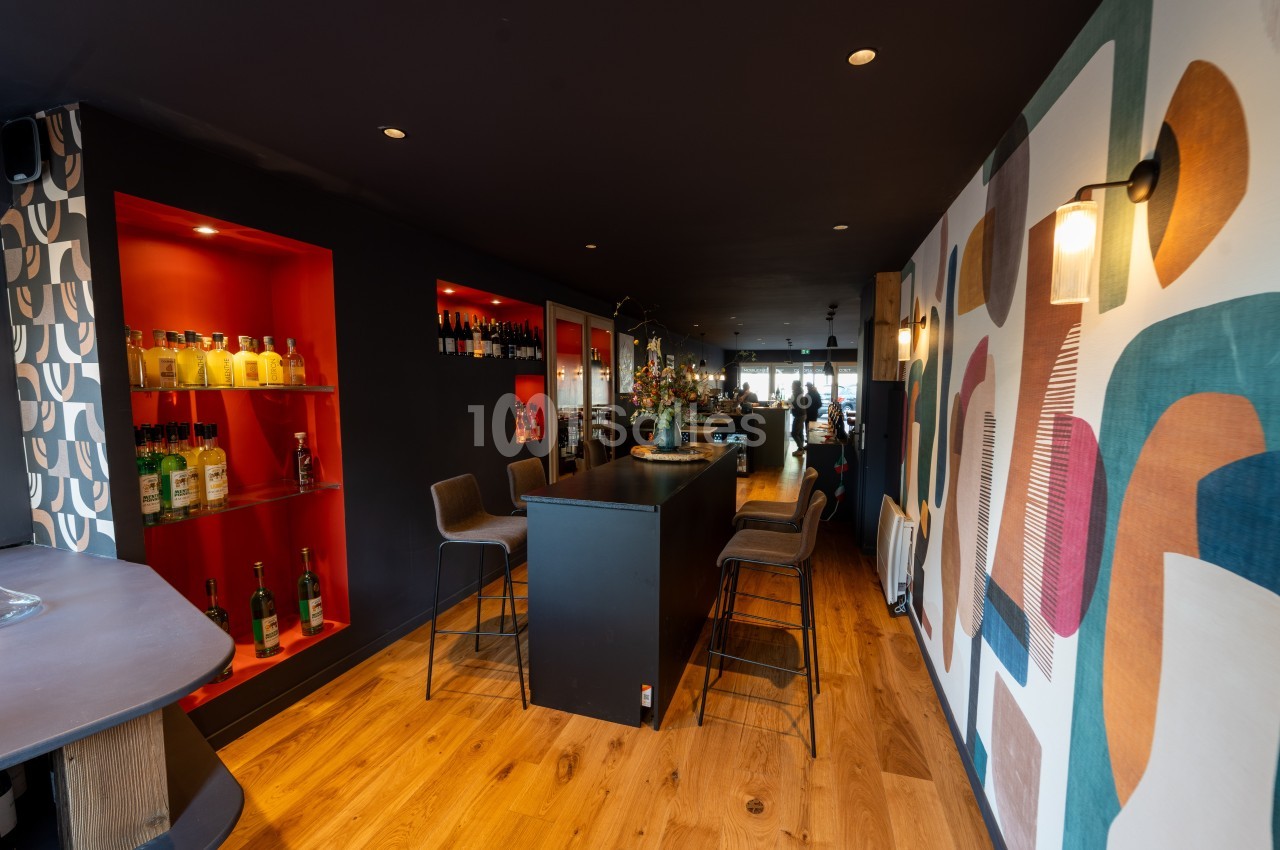 Intérieur d'un bar moderne avec comptoir central, étagères éclairées rouges et décoration murale colorée.