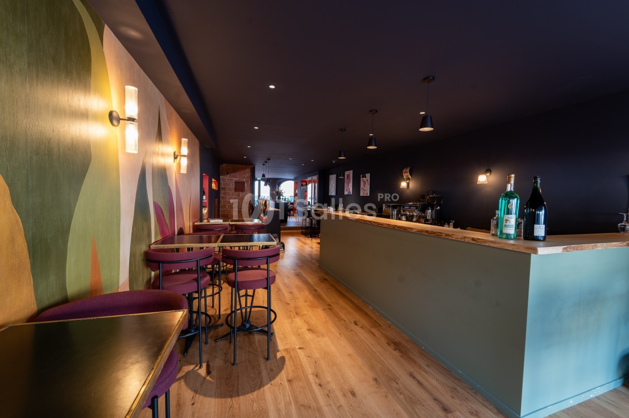 Intérieur d'un bar moderne avec un comptoir en bois, des tables hautes et une décoration murale colorée.