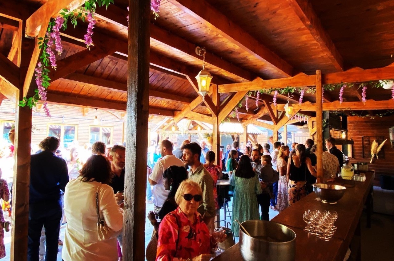 Groupe de personnes réunies dans un espace en bois décoré de fleurs suspendues, éclairé par la lumière naturelle.