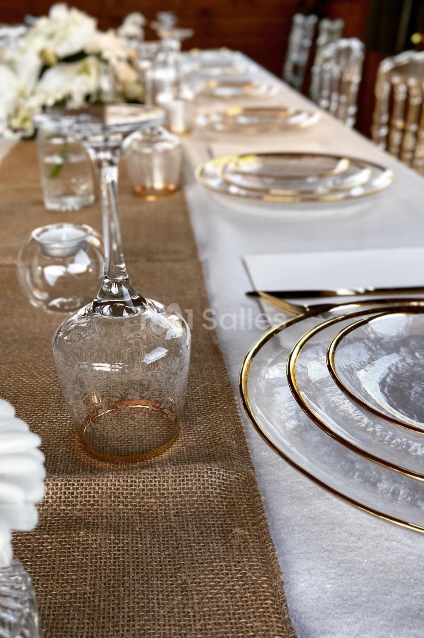 Table élégamment dressée avec des assiettes en verre, des verres à pied et une nappe en toile de jute.
