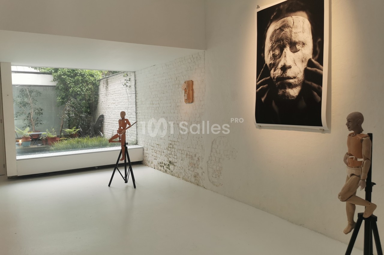 Salle d'exposition lumineuse avec des mannequins en bois et une photographie en noir et blanc accrochée au mur.