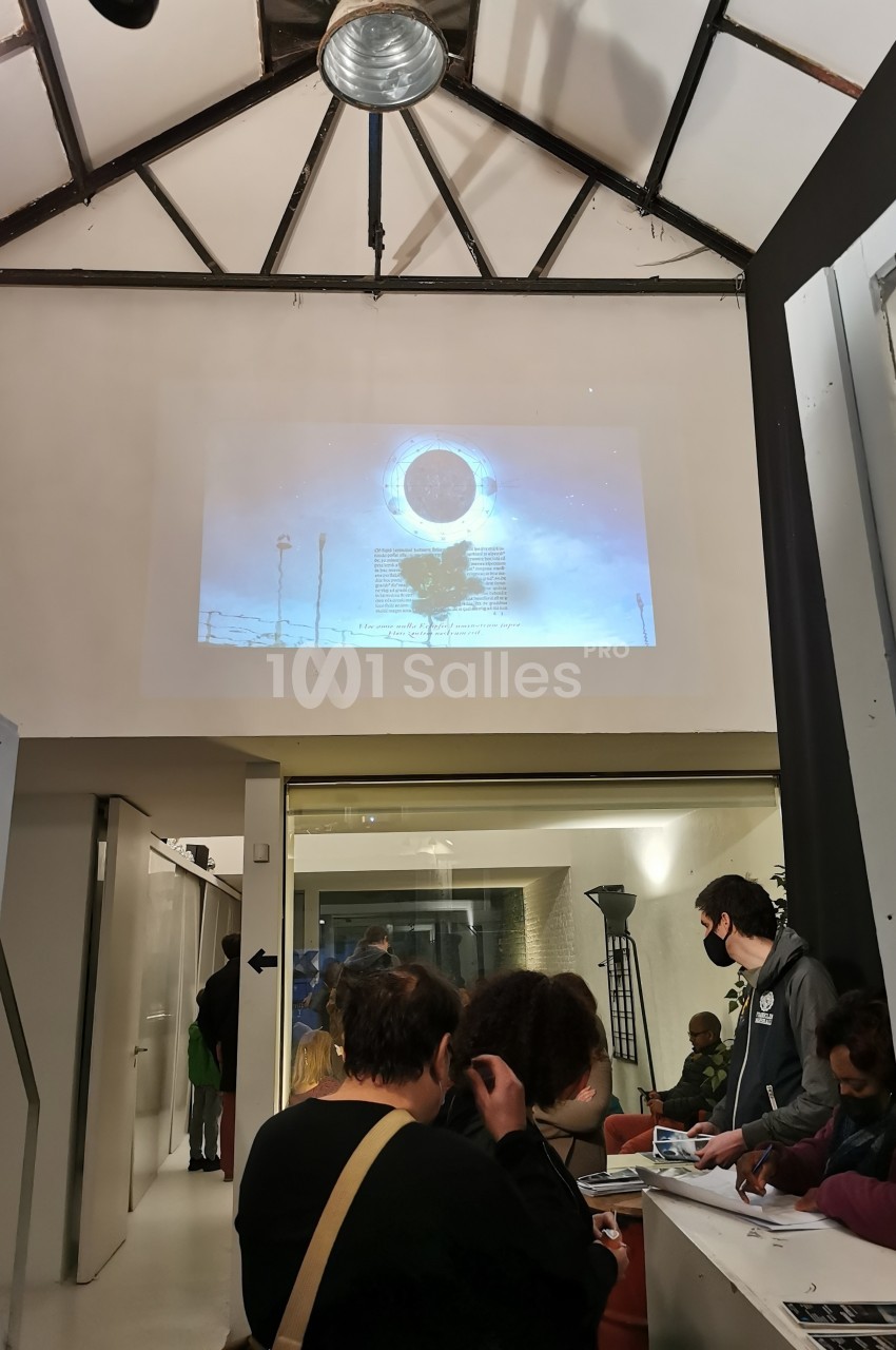 Projection d'une image sur un mur dans un espace intérieur avec des personnes assises et debout en arrière-plan.