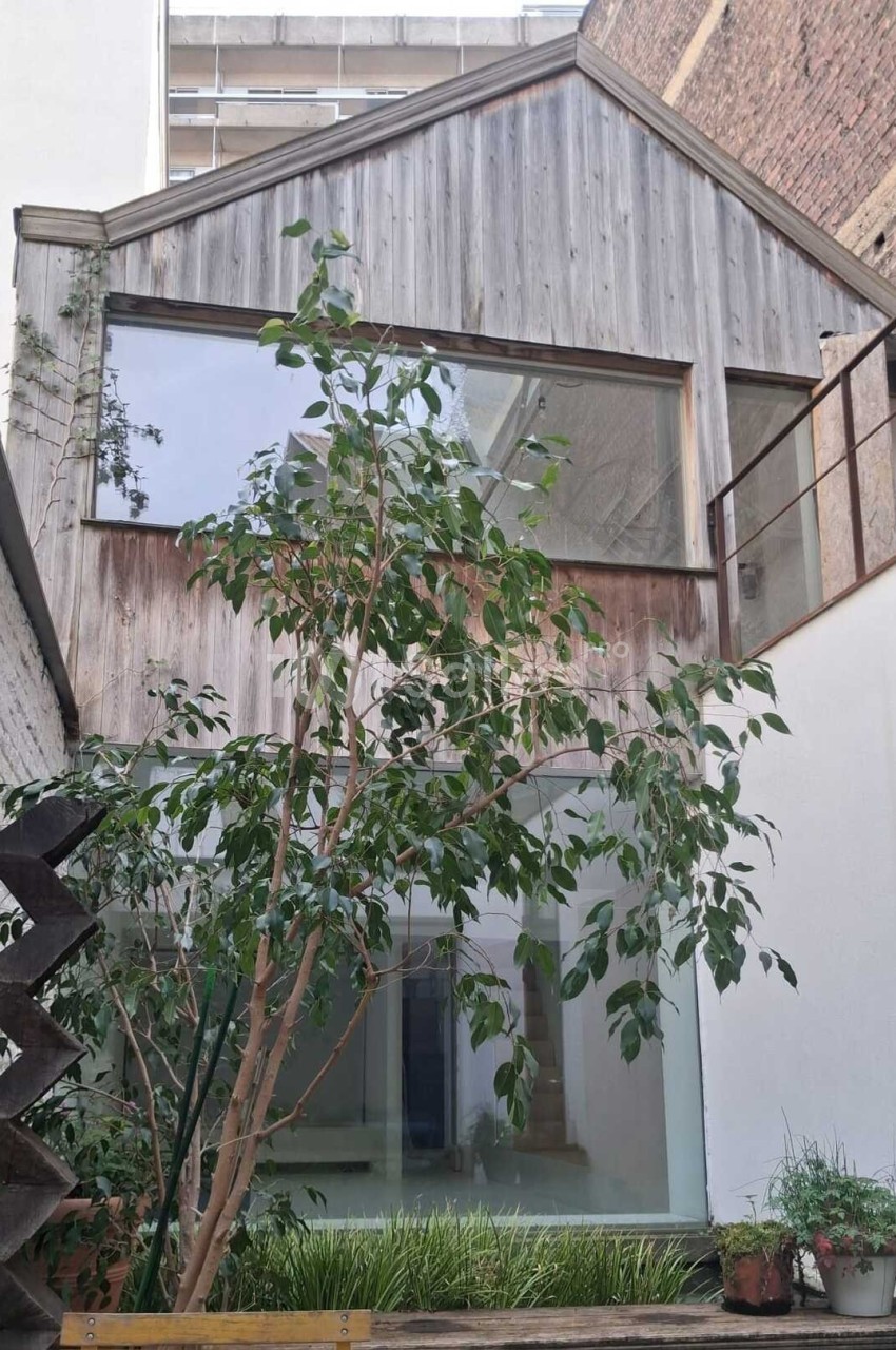 Façade d'une maison moderne en bois avec de grandes baies vitrées, entourée de murs en briques et végétation.