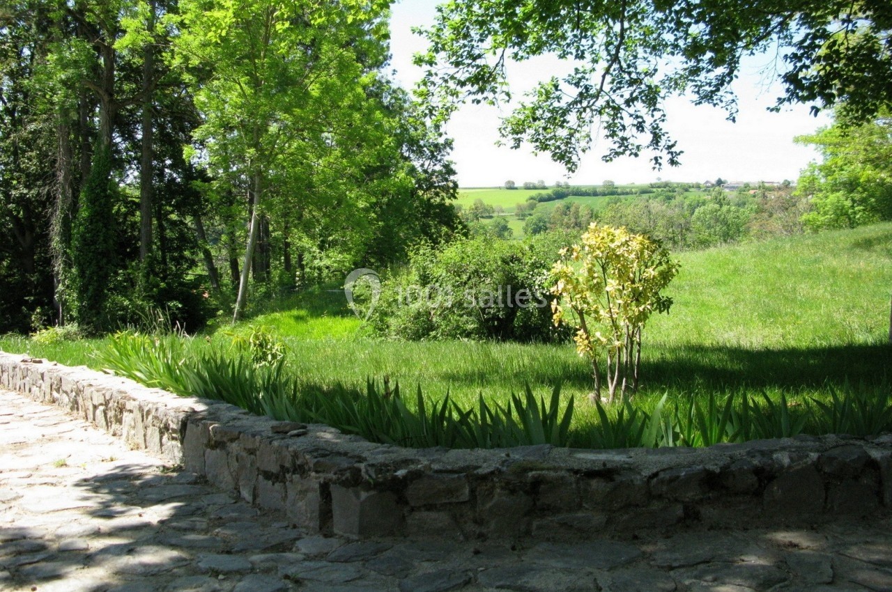 Allée pavée bordée de verdure, donnant sur un paysage de prairie et d'arbres sous un ciel dégagé.