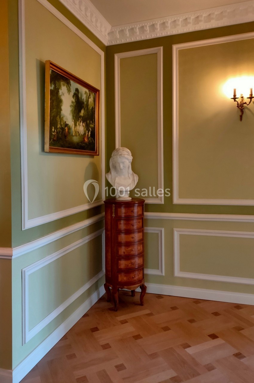 Buste en marbre posé sur une commode en bois dans une pièce aux murs verts ornés de moulures et d'un tableau.