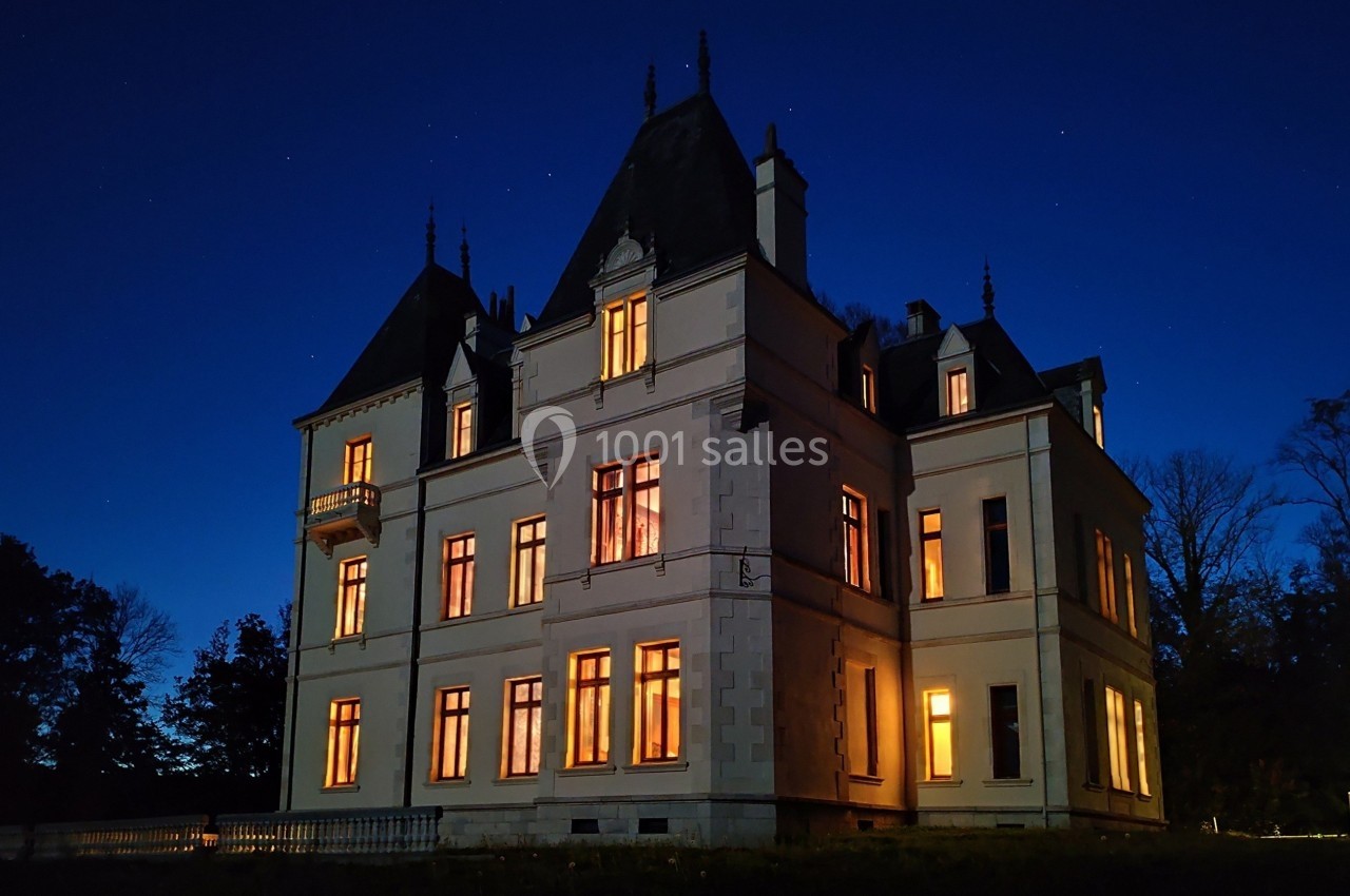 Façade d'un château éclairé de nuit, avec des fenêtres illuminées et un ciel étoilé en arrière-plan.