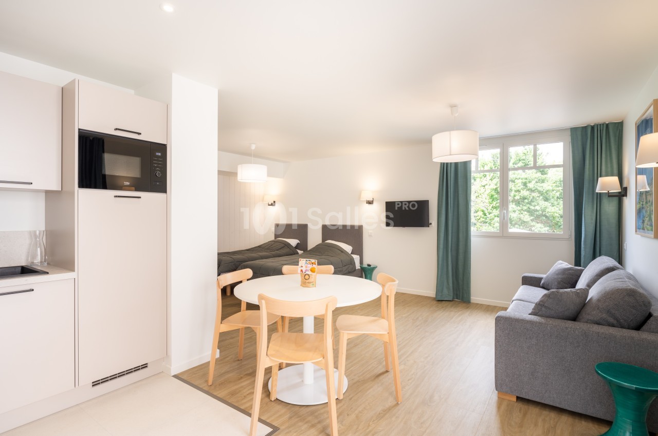 Studio lumineux avec kitchenette équipée, table à manger, canapé, deux lits simples et grande fenêtre donnant sur l…