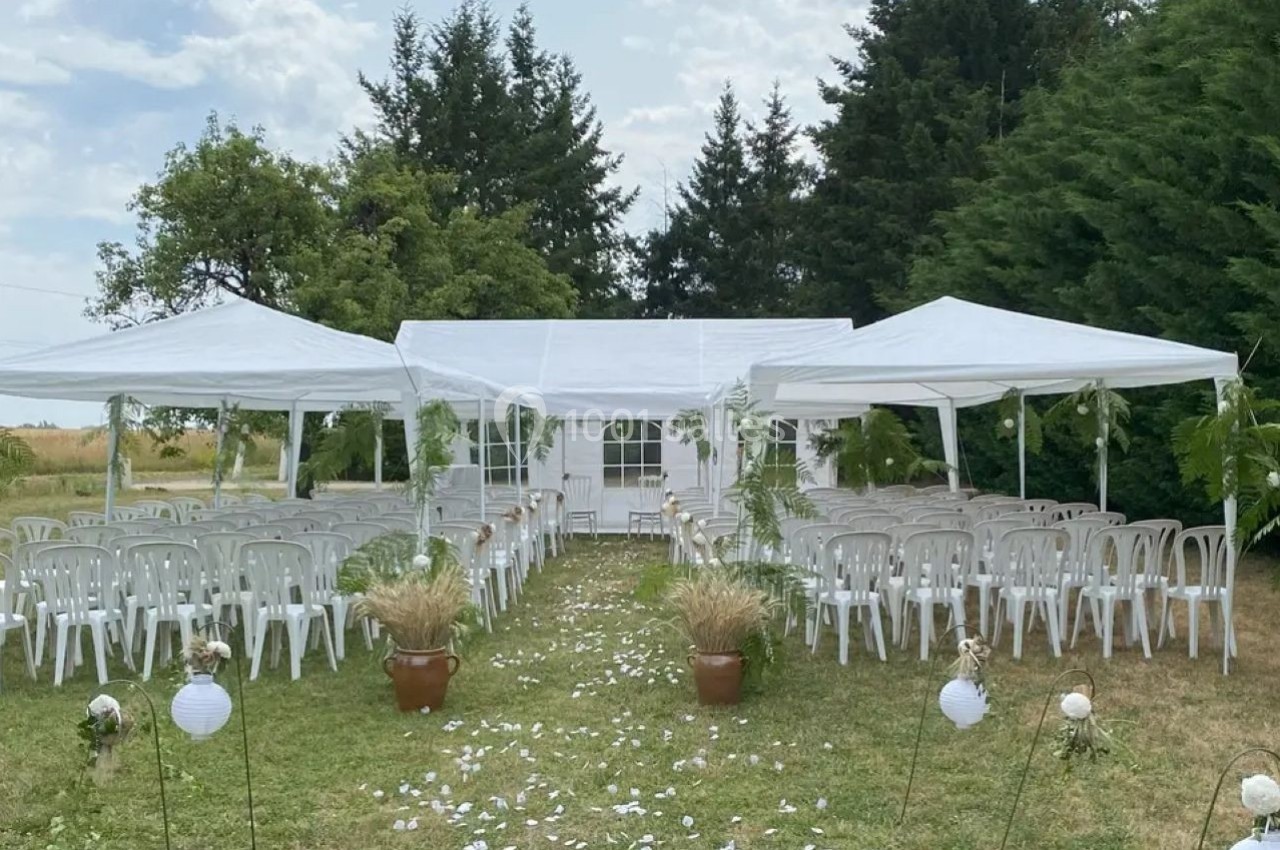 Chaises blanches alignées sous des tonnelles dans un jardin, décorées pour une cérémonie en plein air.