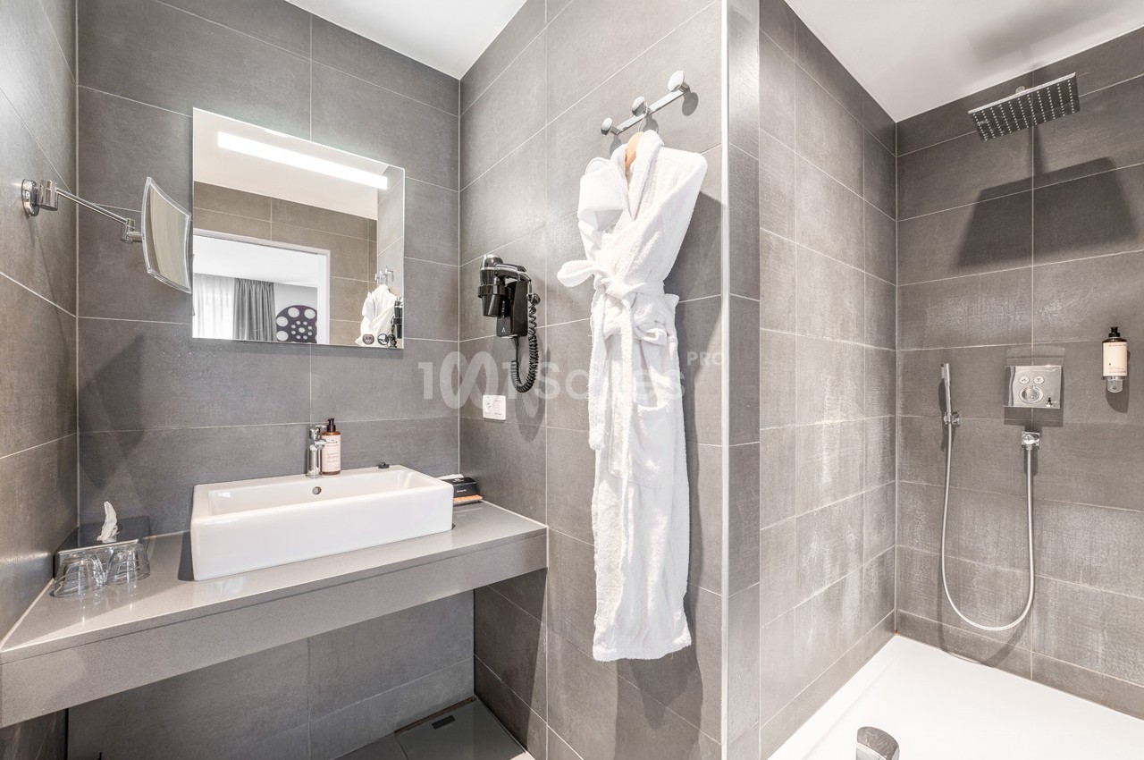 Salle de bain moderne avec douche à l'italienne, lavabo, miroir, sèche-cheveux et peignoir suspendu.